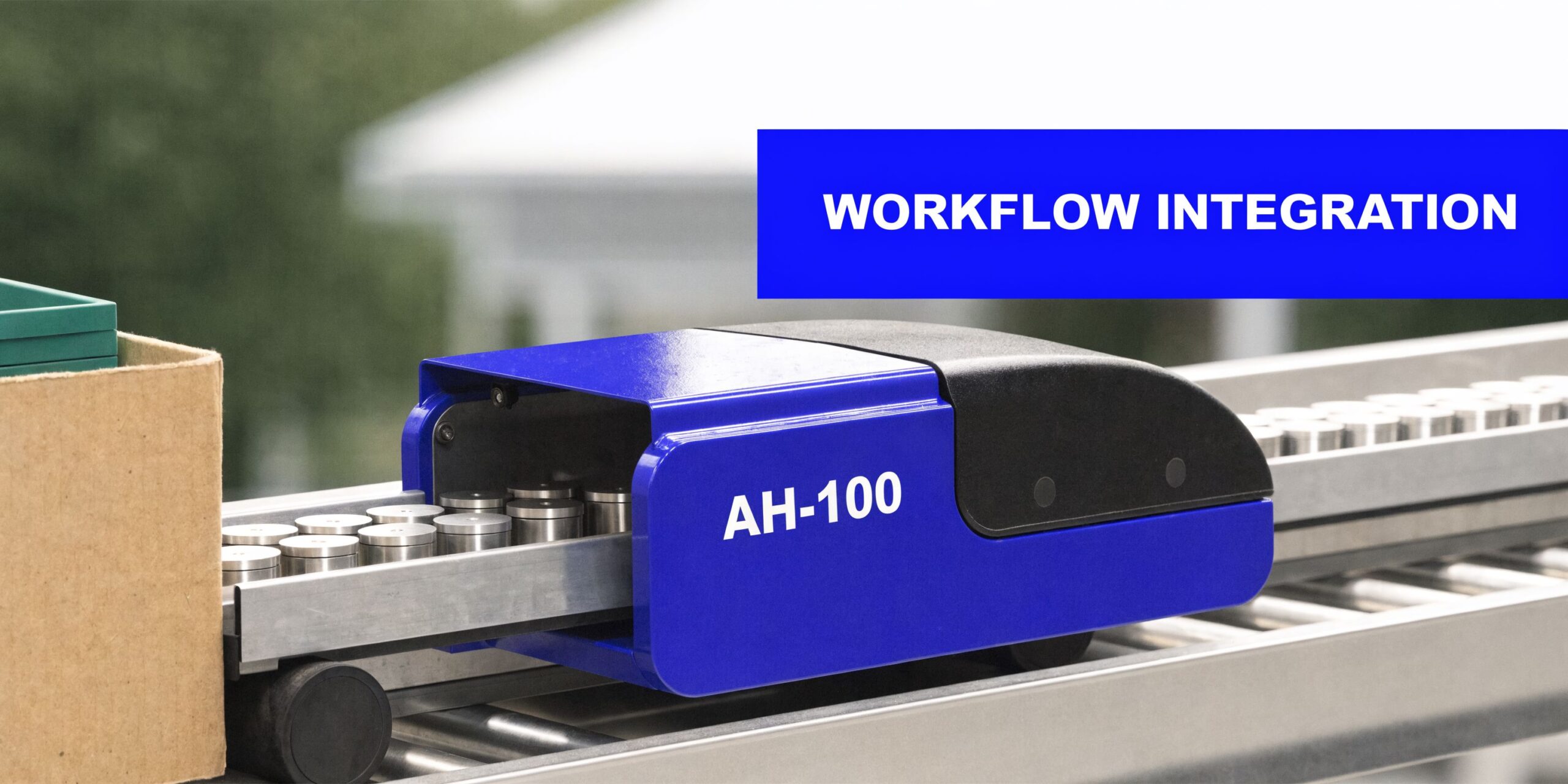 An AH-100 material handling device on a conveyor belt moving metal parts during industrial workflow integration.